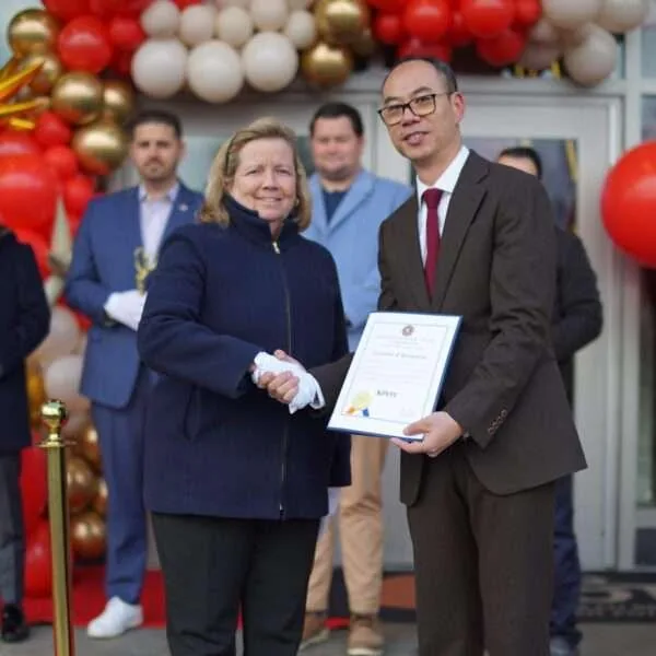 Woman and man shaking hands while holding a KPOT certificate of recognition at an opening event with balloons