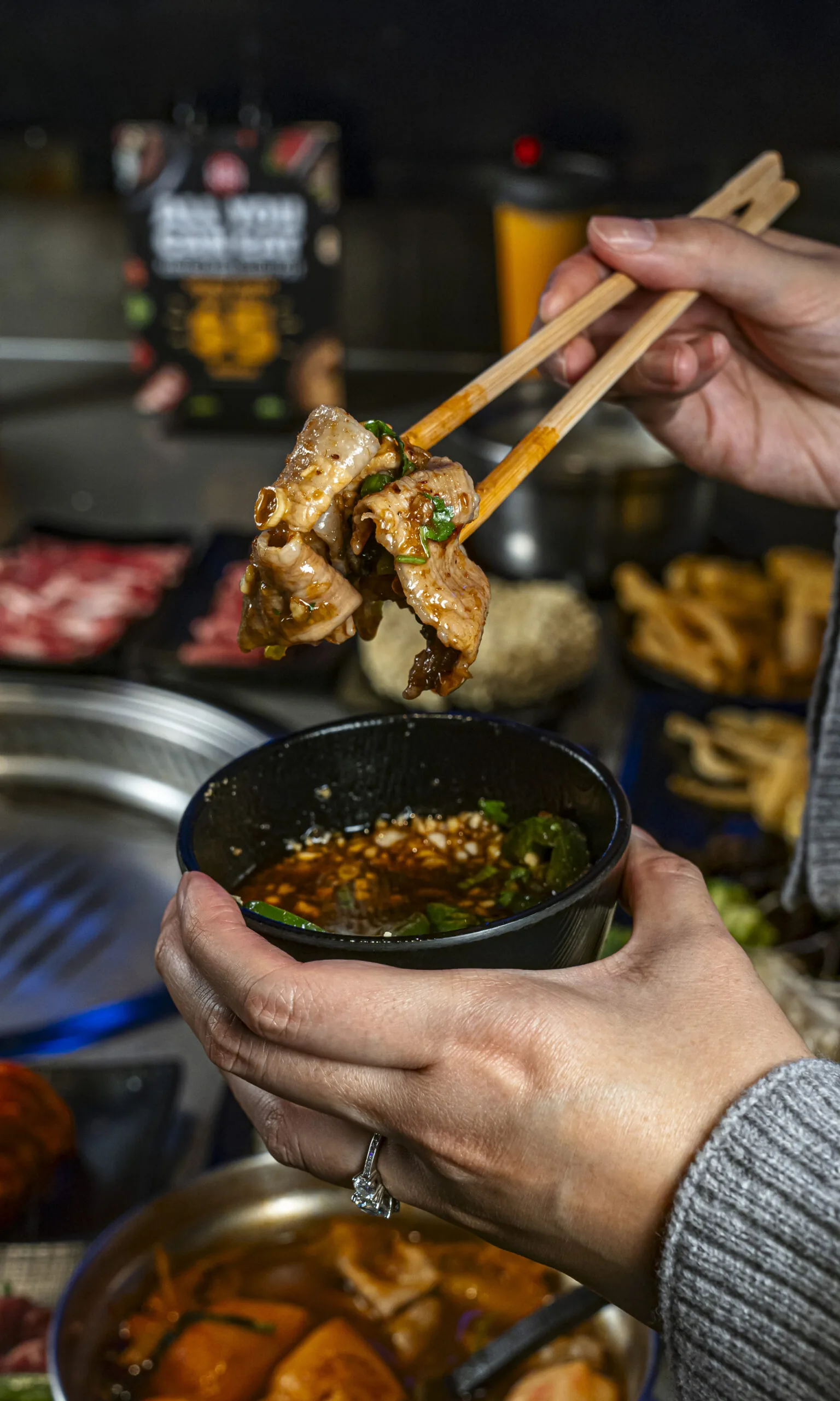 Person dipping grilled meat into sauce at KPOT