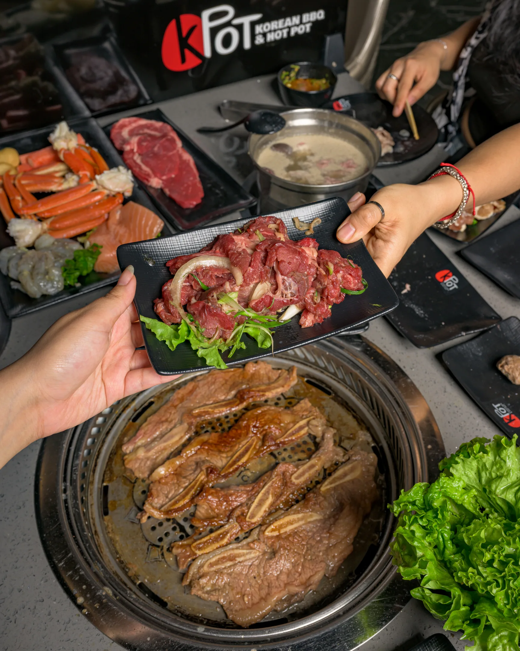 Two people grilling and sharing a plate of steak at KPOT